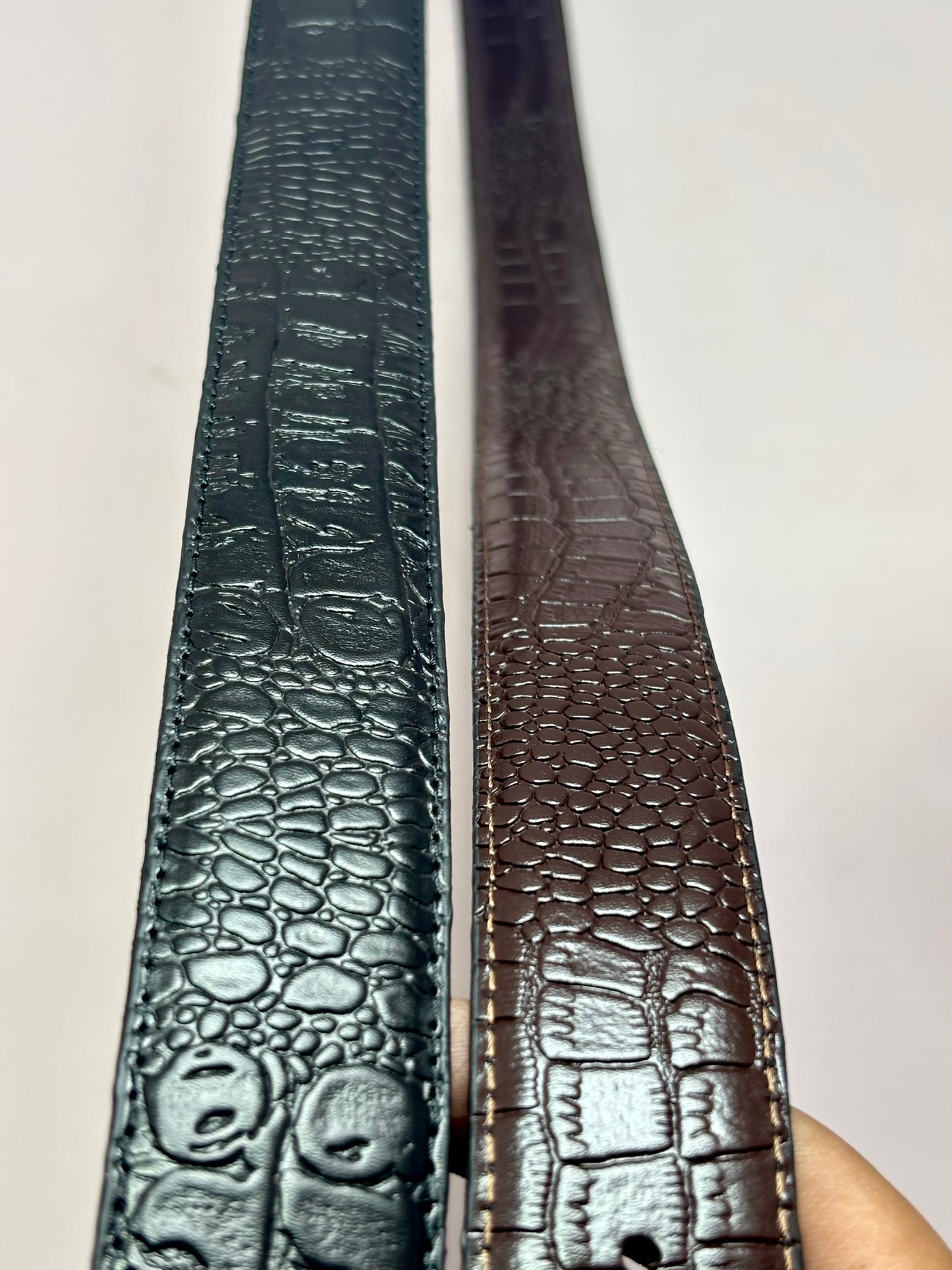 Two leather belts with textured patterns on a light background
