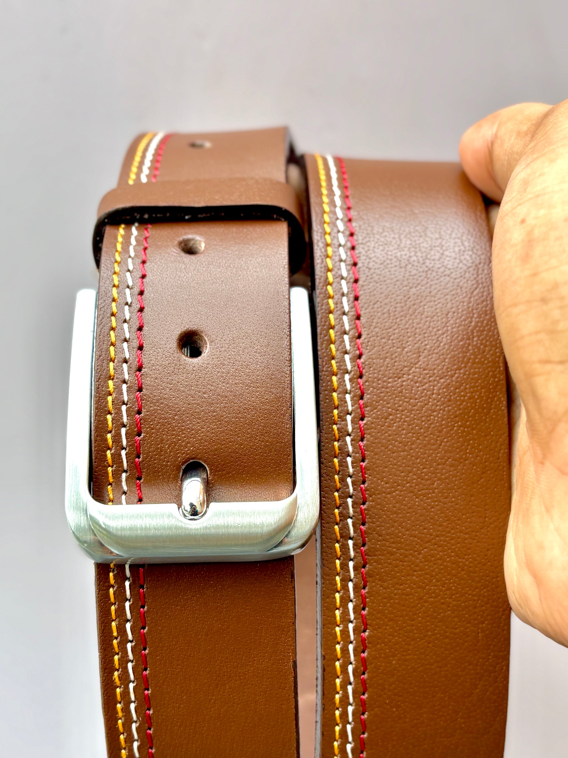 Brown leather belt with white buckle held by a hand on a gray background